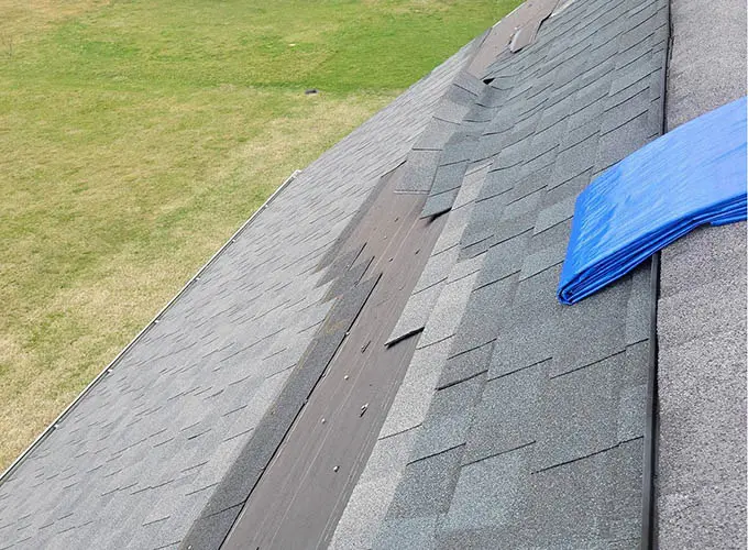 Flint Roofing Contractor servicing a weather damaged asphalt shingle roofing on home in flint prior to roof leak tarping services.