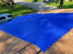 Emergency roof tarping after storm damage from a fallen tree branch on a Michigan home.