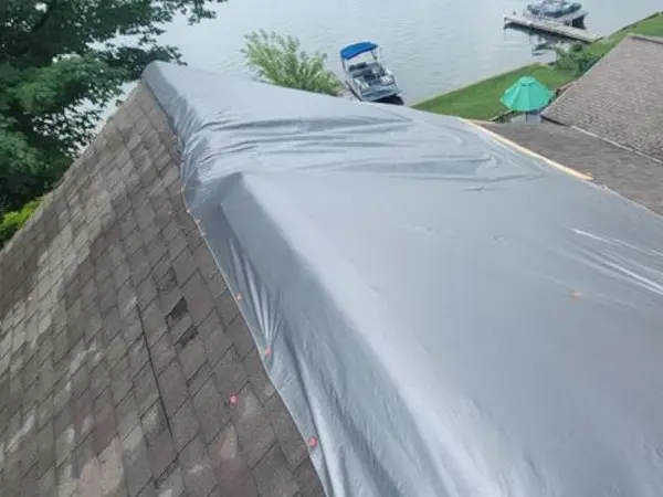 Emergency gray roof tarp installed on a lakeside home after tree damage by Ideal Roofing.